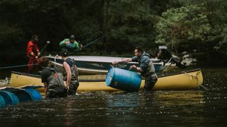 Men standing in a river lift barrels and do manual labor