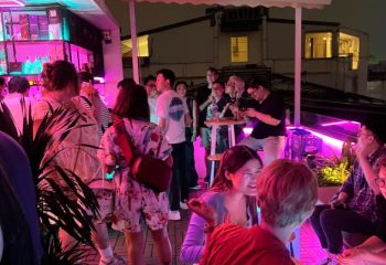 Rooftop bar in Hanoi, Vietnam, with a diverse crowd of people enjoying drinks and socializing under colorful neon lights. Gay travel nightlife.