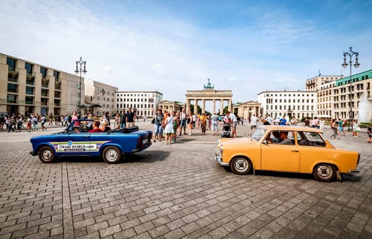 Retro Trabant cars in Berlin, Germany, with the Brandenburg Gate in the background. Queer travel adventure vibes.