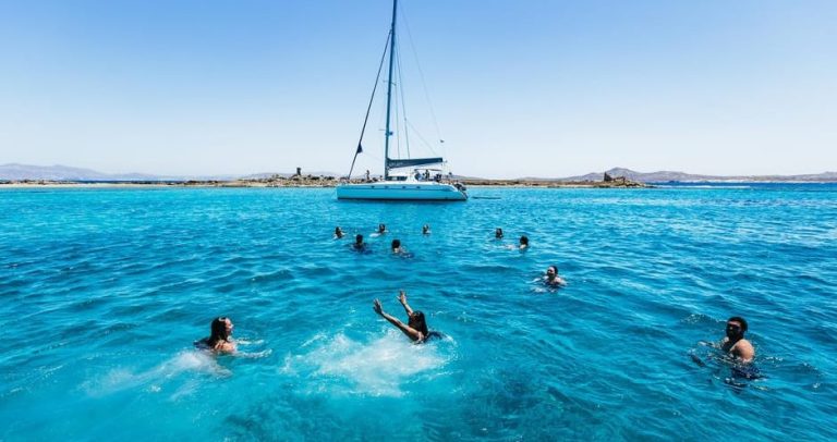 Gay men snorkeling on a yacht cruise from Mykonos to Delos & Rhenia. Turquoise waters, summer sun, and a sailboat in the background.