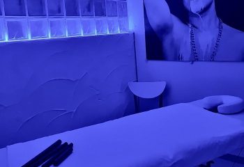 Gay sauna in Sitges. Massage table in blue light, part of a male portrait on the wall. Relaxing spa experience for gay men in Sitges, Spain.