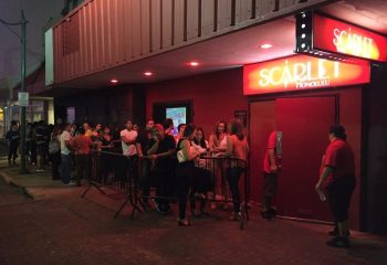 People line up outside Scarlet Honolulu, a gay bar with drag shows. The entrance is red with a bright sign. Gay travel advice.