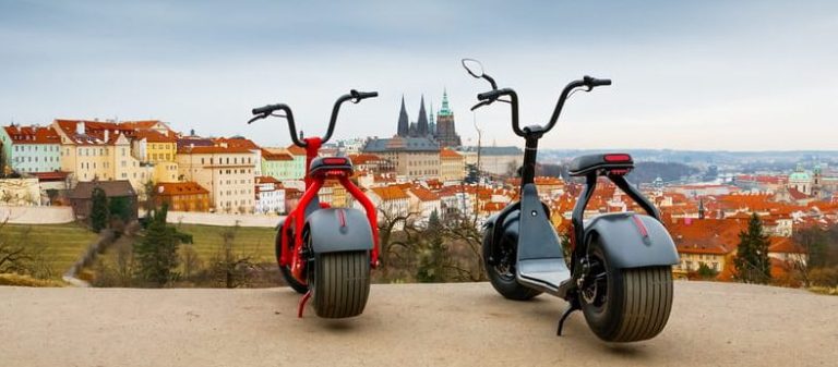 Prague fat tire e-scooter tour. Electric scooters with Prague's skyline. Gay travel adventure in Prague. Fun sightseeing for gay men.