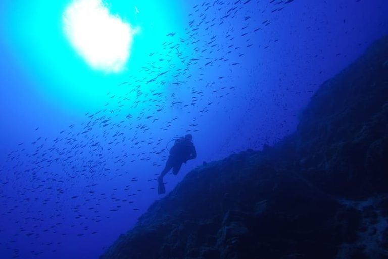 Gay scuba diver explores the underwater world in Santorini, Greece. Enjoy diving adventure with schools of fish and rock formations.