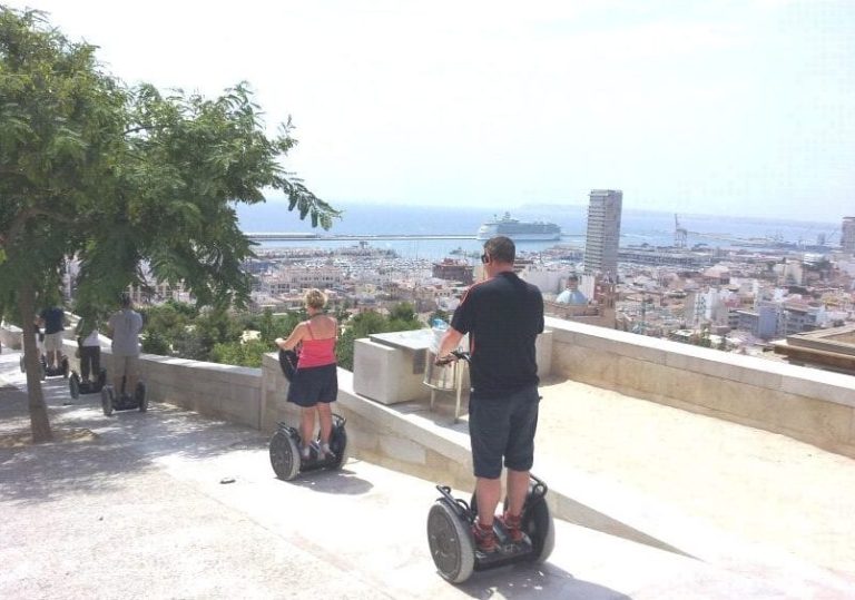 Segway Thrills: Glide through Benidorm's hot spots. People on Segways enjoying city views, cruise ship in background. Gay travel advice.