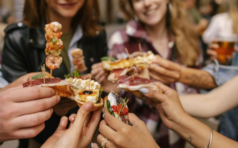 Barcelona Tipsy Tapas Crawl: People holding various tapas. Food tour fun in Spain. Gay travel advice for foodies. Sips & Bites.