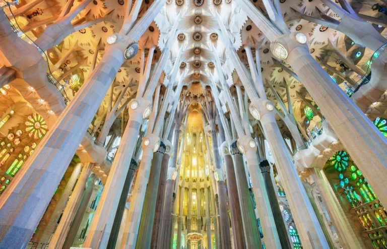 Sagrada Familia interior view. Gaudi's masterpiece in Barcelona, Spain. Tall columns reach towards the ornate ceiling. Stained glass windows add color.