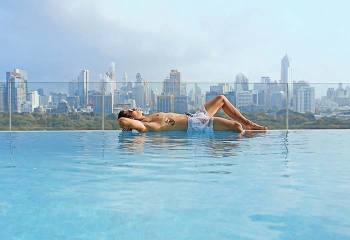 Gay traveler relaxing at SO/ Bangkok hotel's infinity pool. Bangkok skyline view. Popular gay hotel for gay men travel in Thailand.