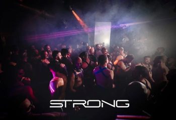 Gay cruise club STRONG in Madrid. Crowd of men in harnesses dancing in a dark, smoky club with laser lights. Gay travel nightlife.