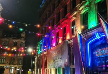 Manchester's Sub 101 nightclub, a gay travel destination, is lit with rainbow colors. Pride flags and string lights adorn the building's exterior.