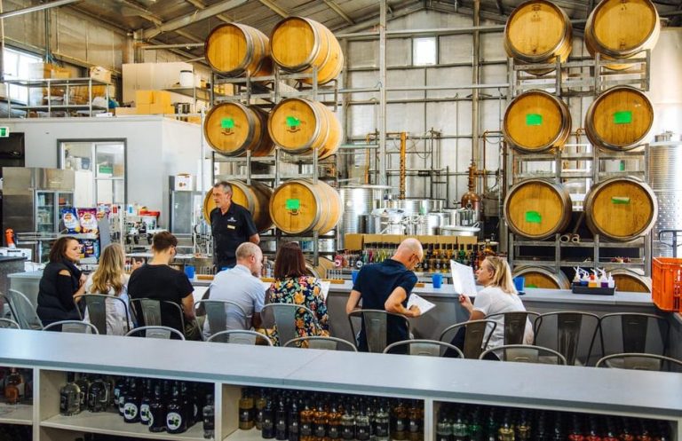 Gay-friendly Hunter Valley wine tour. Group at a tasting; barrels stacked high. Sips, scenery, and sass on a spirits tour.