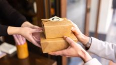 Close-up image of the hands of a waiter giving two small brown takeout boxes to a customer in a restaurant