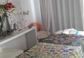 Thai holistic massage room in Gran Canaria. Massage bed with floral pattern, white curtains, and flowers. Gay travel wellness.