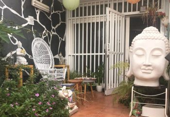 Holistic Thai massage entrance in Gran Canaria. Buddha statue, peacock chair, and plants create a serene spa atmosphere. Gay travel.