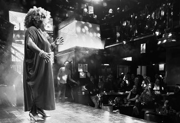 Black and white shot of drag queen performing at The George gay club in Dublin. Audience members are watching the stage show.