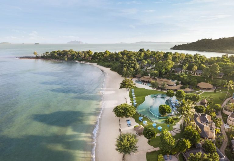 Aerial view of The Naka Island, a luxury gay-friendly hotel in Phuket, Thailand. Features a beach, pool, villas, and lush greenery.