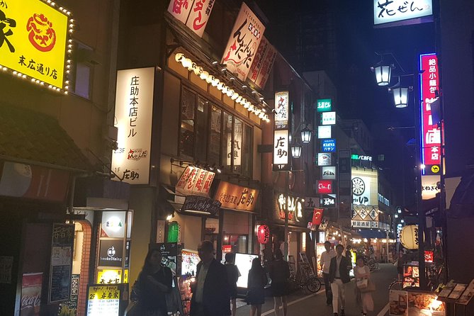 Tokyo Gay Tour: Night street scene with illuminated signs & people. Experience a Ramen tasting tour with mini bowls in Japan's vibrant gay district.