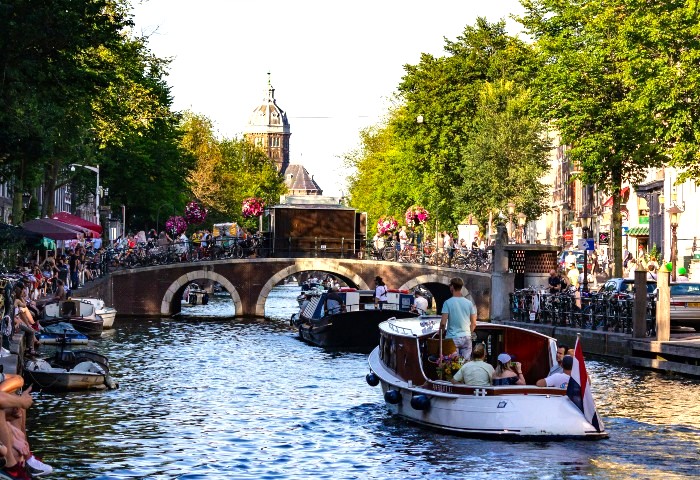 Amsterdam canal scene. Boats on water, bridge with bikes, and buildings. Gay-friendly spots in Amsterdam's city centre.