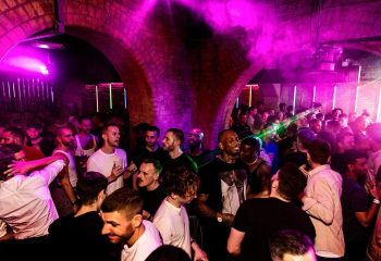 CIRCA The Club, a top late-night gay club in London. Go-go boys and patrons enjoy the vibrant nightlife under purple lights and arched ceilings.
