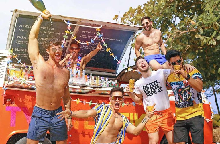 Gay travelers at a top luxury beach hotel in Koh Samui, Thailand. Group of shirtless men celebrating with drinks at an outdoor bar. Tropical vacation.