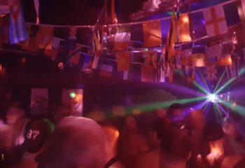 Inside TRADE Club Sydney: Gay men dance under international flags and club lights. Nightlife scene for gay travel advice.