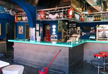 Interior of Tubos Bar, a gay club in Gran Canaria, featuring a blue bar, bottles, and red stools. Gay travel destination.