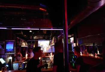 Interior of Tubos Gay Bar in Gran Canaria. People at the bar, drinks, and a projector screen. Nightlife scene. Gay travel advice.