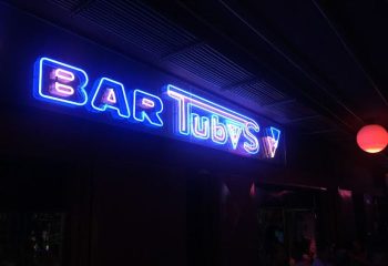 Neon sign for Tubos Bar, a gay club in Gran Canaria. The sign is bright blue and pink, and the bar is dark and inviting. Gay travel.