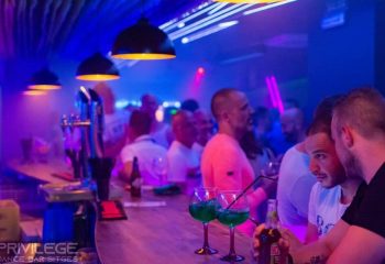 Vertigo Dance Bar, gay club in Sitges. Men at the bar with drinks, enjoying the vibrant nightlife. Blue and purple lighting.