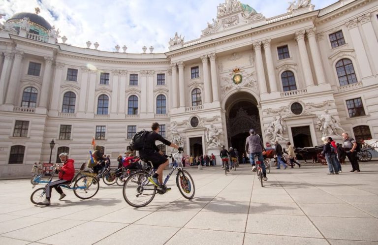 Gay men's Vienna bike tour through history and hotspots. Bicyclists in front of Hofburg Palace, a historic landmark. Vienna travel.