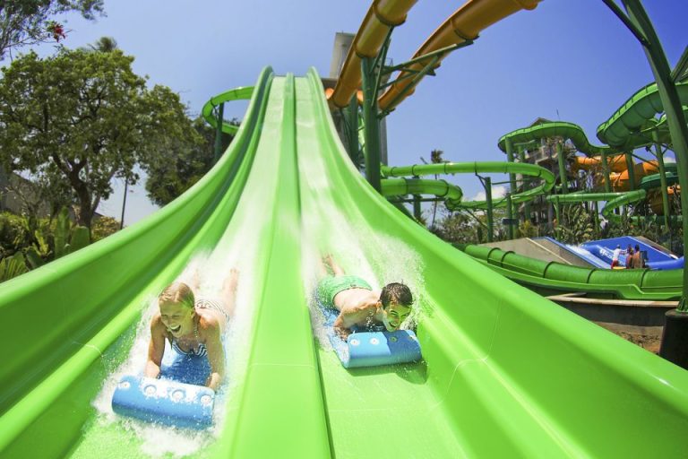 Waterbom Bali WaterPark: People on a green waterslide with blue floats. A fun gay travel destination with instant entry tickets for a 1-day visit.