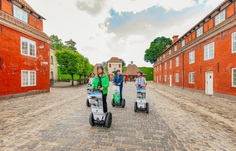 Copenhagen Segway Experience: Group of gay men explore the city on Segways, gliding past historic red buildings. Wheels and Wonders tour adventure.