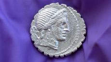 A close up of a silver coin with a Roman face