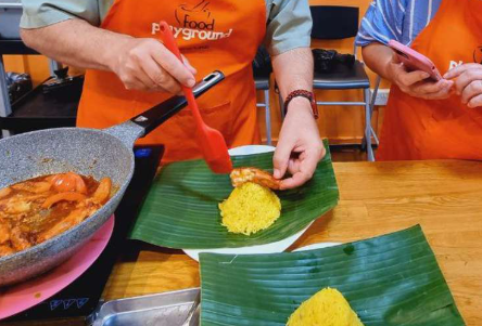 Hands-on cooking class: Chef plating yellow rice and shrimp on banana leaf. Cultural immersion experience for gay men travelers. Food playground.
