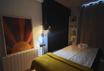 Gay spa massage room in Dublin. Massage table with yellow blanket, sun art, black wall, and shelf. It's Always Sunny, a gay travel tip.