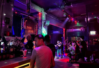 POC Bar, a lively gay bar in Phnom Penh. People are standing at the bar and socializing in the dimly lit, colorful space.