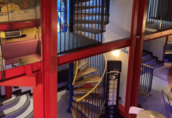 Interior view of The Boilerhouse gay sauna in Dublin. Red beams, spiral staircase, and elevator panel are visible. Gay travel.