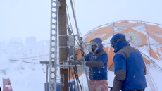 Two researchers drill into a glacier